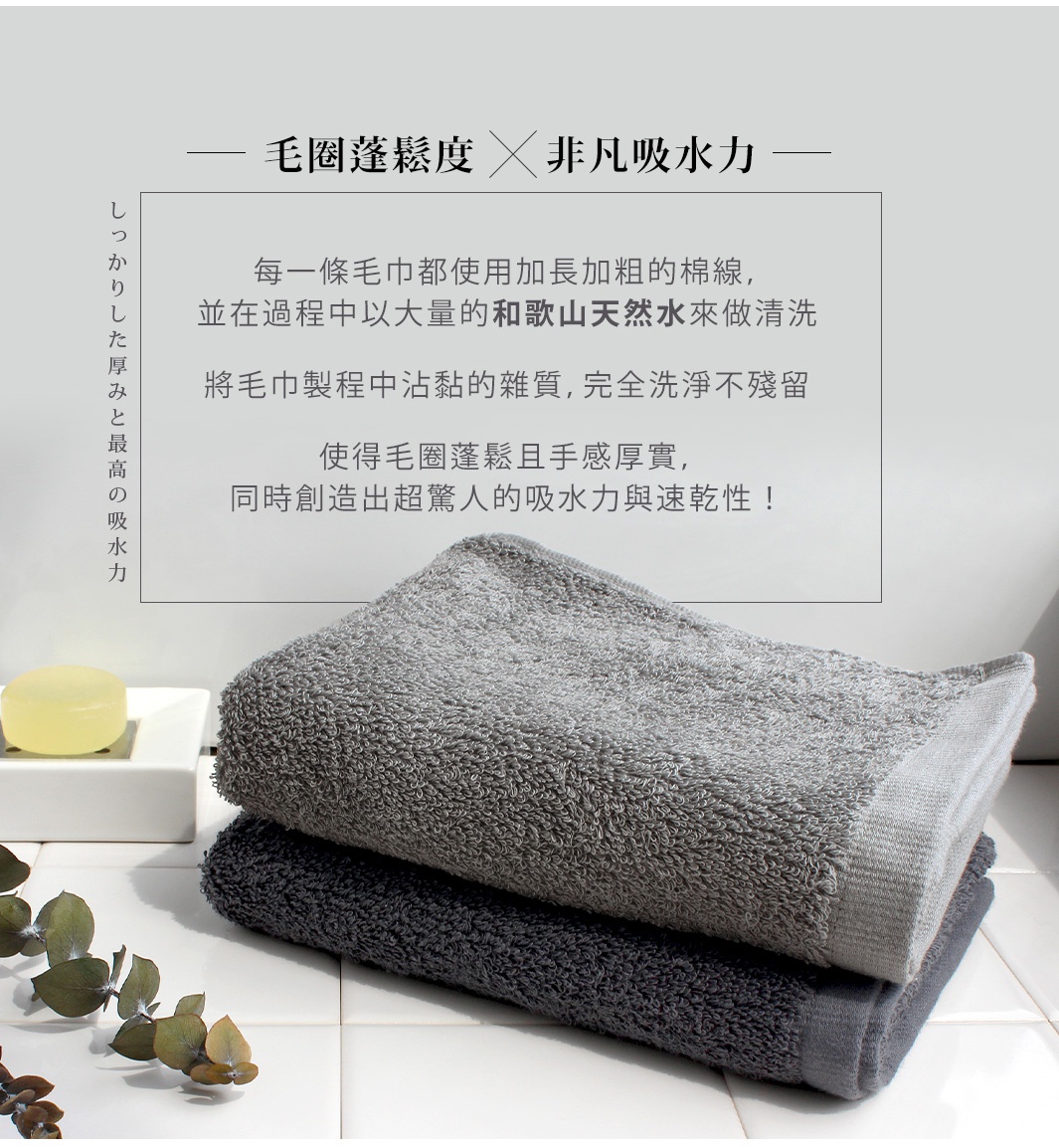 兩條疊放的毛巾，上方是淺灰色，下方是深灰色，毛巾質地蓬鬆，表面有細密的毛圈，背景是白色格紋瓷磚，左側有日文說明文字。