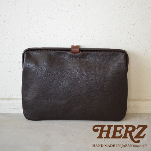 深棕色職人手作皮革Organ手拿包，簡約設計，帶有小巧的皮質搭扣，展現皮革自然紋理。