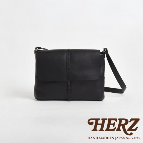 日本HERZ 職人手作黑色皮革細扣帶馬鞍包，包款正面有細緻縫線與扣帶設計。