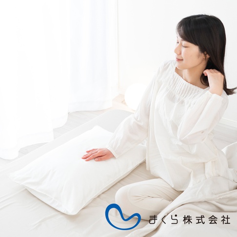 白色棉絲混紡枕套，柔軟平整，搭配一名身穿白色長袖上衣的女子，她坐在一張床上，手放在枕頭上。