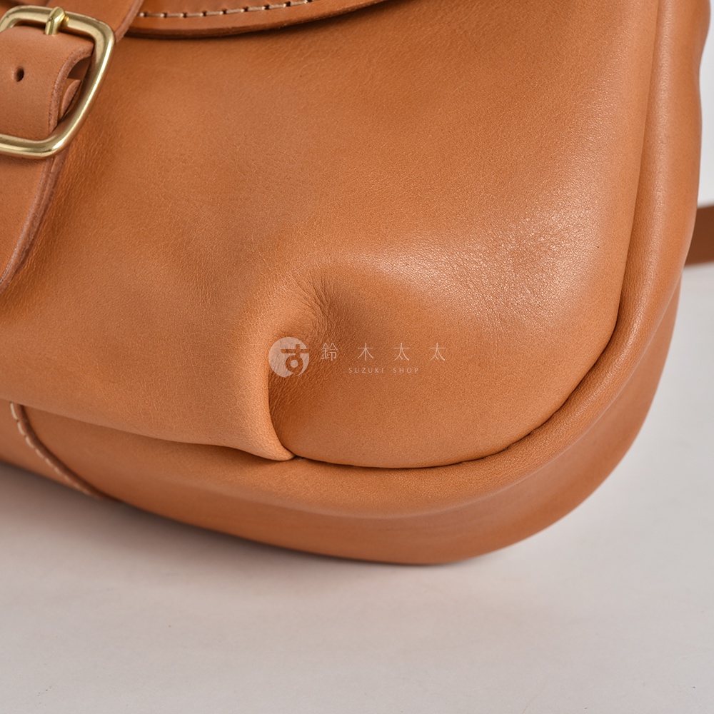 日本HERZ職人手作Stare皮革休閒旅行馬鞍包CK-20的局部特寫，展現包包一角的圓潤弧度與皮革自然紋理，品牌Logo「鈴木太太」及其英文「SUZUKI SHOP」清晰可見。
