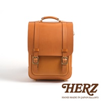 職人手作皮革小學生書包，展示色為淺棕色，採用高品質皮革製作，配有兩個金屬扣環及頂部提把，設計簡潔實用。