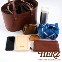 職人手作咖啡色皮革束口手提包，內含深棕色束繩內袋，搭配同色系皮革零錢包、長夾、手機、書籍及藍色印花布包，另有一支銀色保溫瓶。