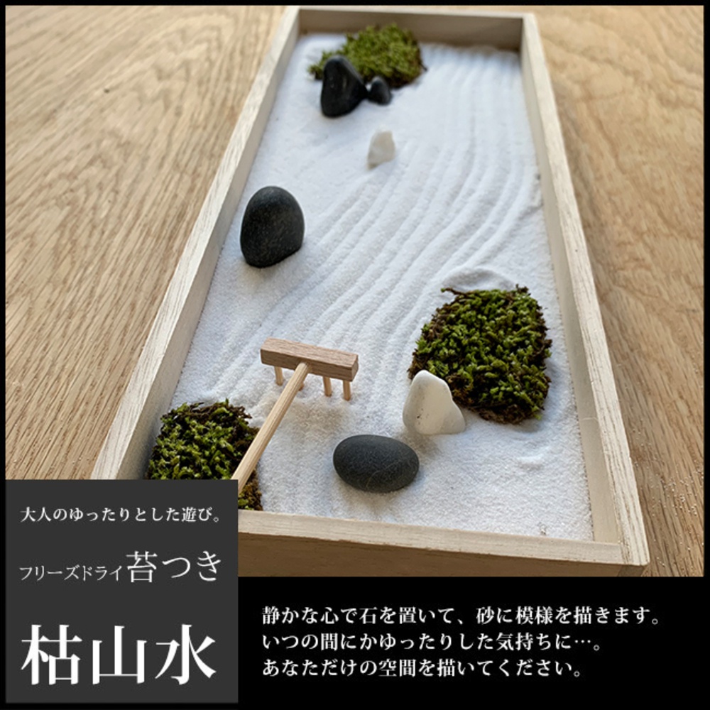 長方形淺木框內，鋪設白色細砂，砂上耙出波浪紋。散置數顆黑色、白色鵝卵石及簇狀深綠色苔蘚，一旁有迷你木耙。