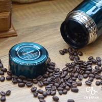 深藍色城市咖啡保溫杯，杯蓋上有「Qahwa Portland」字樣，杯身散落著咖啡豆，保溫杯內部也裝有咖啡豆。