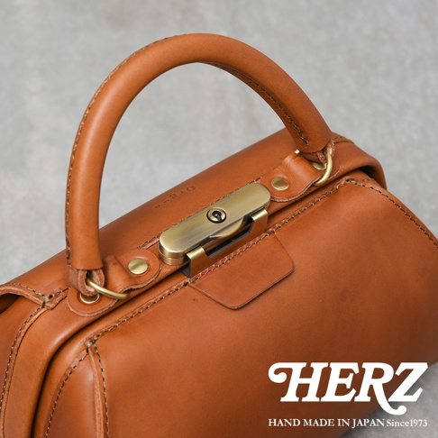 職人手作咖啡色皮革兩用口金手提包，帶有復古金色金屬鎖扣和圓弧形提把，皮革表面有細緻縫線與壓印品牌Logo。