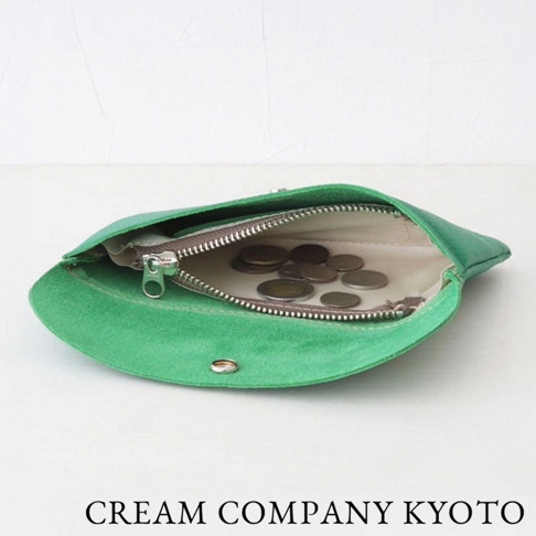 一隻綠色麂皮製成的多功能收納包，拉鍊部分可見內部裝有零錢。收納包以開放式方式展示，底部有金屬按扣。