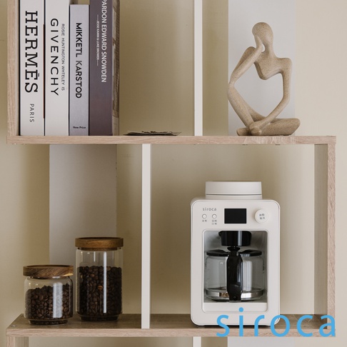 白色 SC-A3520 自動研磨咖啡機，上方有白色頂蓋和黑色觸控螢幕，前面有透明玻璃咖啡壺，下方有黑色底座，右側有兩個按鈕，置於木紋層架上。