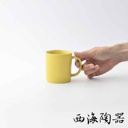 黃色陶瓷馬克杯，杯身圓潤，帶有弧形提把，由手持拍攝，背景為白色。
