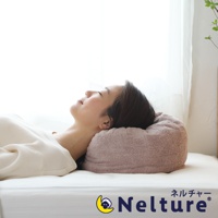 一位女子仰躺在床墊上，頭部枕於一個粉紅色、觸感類似毛巾的甜甜圈形狀枕頭，枕頭外層為絨毛材質，呈現立體環狀。