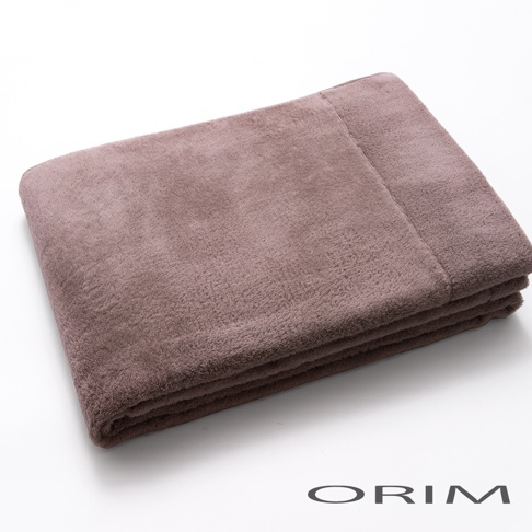 一條對折的淺褐色毛絨毛毯，材質柔軟，邊緣有縫線，底部有「ORIM」字樣。