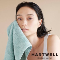 一位女性使用一條淺綠色、柔軟的毛巾輕柔地擦拭臉部。