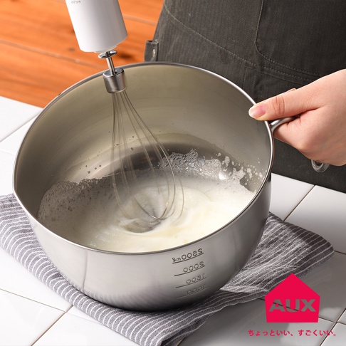 一個附有手把的銀色不鏽鋼攪拌鍋，鍋內有打發的白色泡沫，一個手持白色電動攪拌器正在攪拌。鍋壁外側有刻度標示。