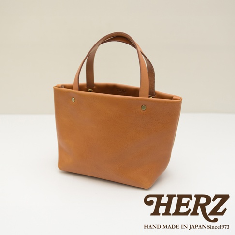 酒紅色皮革製成的極簡托特包，配有兩條皮革提把，包身正面有兩個鉚釘裝飾。