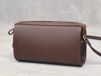 咖啡色皮革製成的拉鍊單肩包，包身呈現圓筒狀，側面有縫線裝飾，附有皮革背帶與金屬掛環。