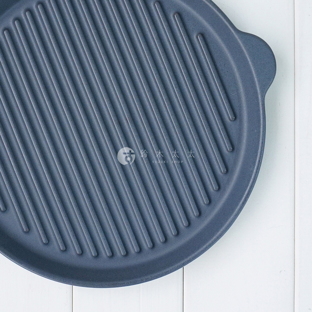 The chef 多功能耐熱陶製萬用波浪圓烤盤 S，深藍色陶製烤盤，表面有規則的波浪紋路，右側有圓形把手，置於白色木紋背景上。