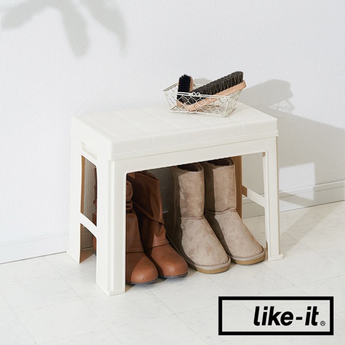 米白色塑膠玄關穿鞋收納椅，上方擺放著一個金屬網籃，籃內有兩支不同大小的清潔刷。椅子下方收納著四雙靴子，包括兩雙棕色皮靴和兩雙米色麂皮靴。