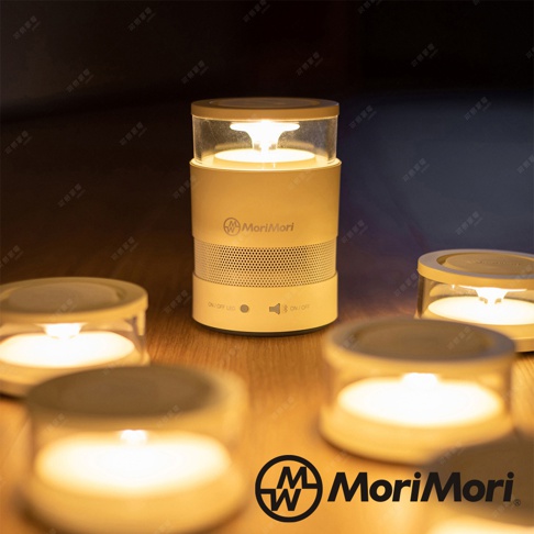 松本素白的 LASMO 燭光氣氛音響，圓柱形設計，頂部為透明燈罩，內部有模擬蠟燭火焰的燈光。音響主體為白色，中間有網狀喇叭孔，底部有「ON/OFF LED」和藍牙圖示按鈕。周圍擺放了數個較小的同款燭光燈。