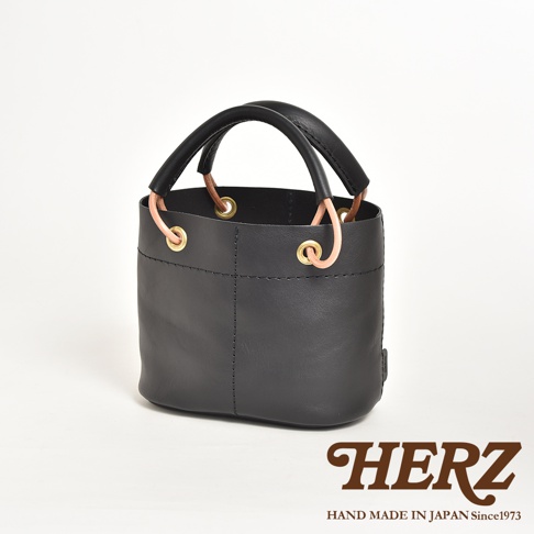 黑色皮革水桶包，配有加厚皮革提把、黃銅孔眼及連接繩。