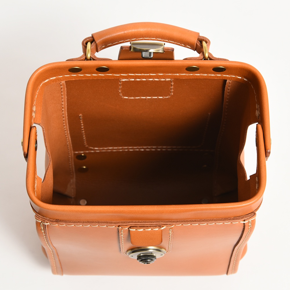 職人手作皮革迷你後背醫生包，採用淺棕色皮革製作，配有金屬鎖扣和提把，邊緣縫線清晰可見，內部空間寬敞。