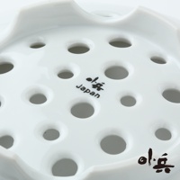 白色美濃燒多用蒸盤，表面佈滿大小不一的圓孔，材質為陶瓷，盤緣有波浪狀設計，盤面上印有黑色日文及「Japan」字樣。