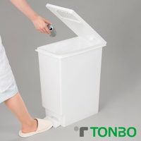 白色塑膠推蓋踩踏式垃圾桶，內部有垃圾袋，垃圾桶前方有踩踏板，顯示使用者正將鋁罐投入。
