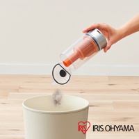 手持吸塵器集塵筒傾斜，將灰塵倒入米白色垃圾桶，集塵筒為透明塑膠材質，內有橘色濾網與吸管。