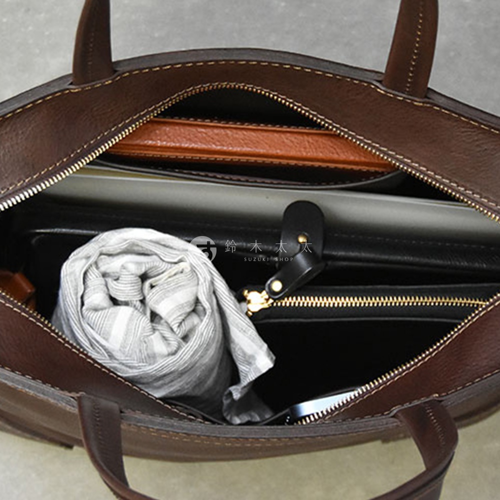 深棕色皮革托特包，內部展示，可見一個捲起來的灰色條紋圍巾，以及黑色和棕色的隔層。