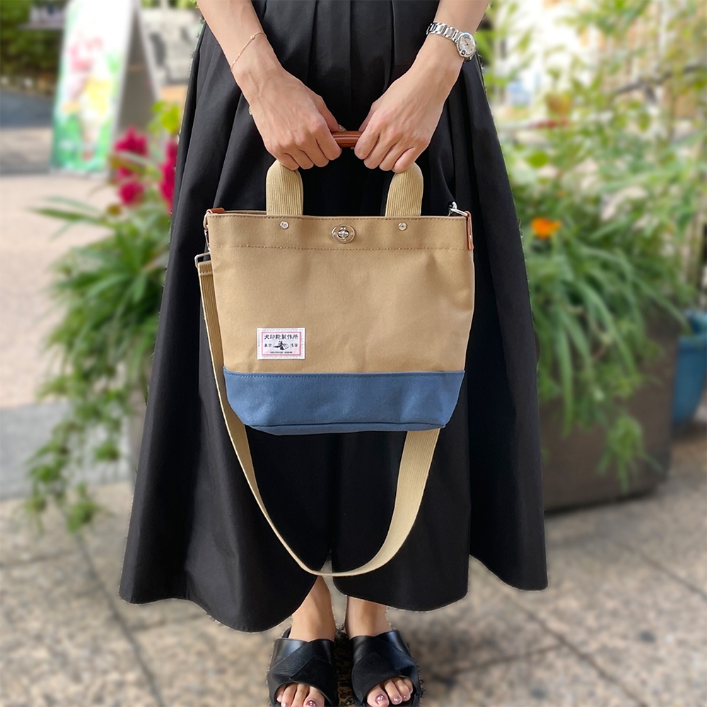 犬印純棉帆布兩用雙色托特包，主體為卡其色，底部為藍色，配有皮革提把和可拆卸的帆布長背帶，包中央有品牌標籤。