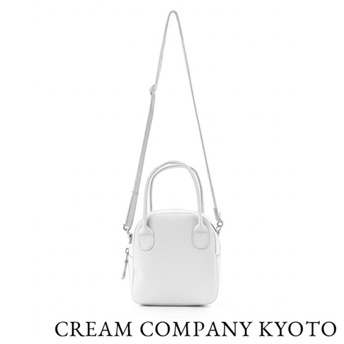 白色CREAM COMPANY KYOTO品牌皮革手提兩用貝殼包，具備簡約圓潤外型、雙提把設計及可拆卸式肩背帶，包身材質為輕量牛皮革，下方標註品牌名稱。