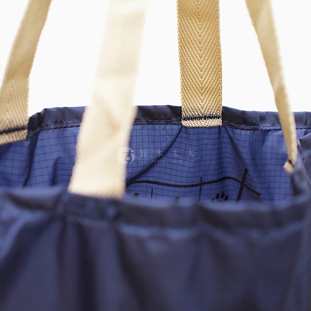 深藍色環保折疊收納購物袋，尼龍材質，配有米白色織帶提把。袋內印有細密的格紋和品牌標誌。