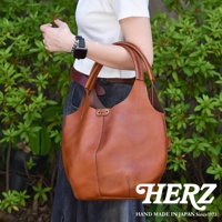 這是一個棕色皮革製成的圓形肩掛托特包，包身有明顯的縫線裝飾，提把為皮革材質。