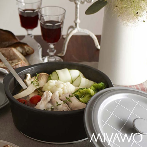 黑色陶土湯鍋內盛有雞肉、花椰菜、櫛瓜、蘑菇和番茄，配有銀色鍋蓋，鍋蓋上印有白色網格紋和品牌標誌。