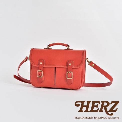 紅色皮革手提/斜肩兩用包，具備兩個前袋和金屬釦環，風格簡約。