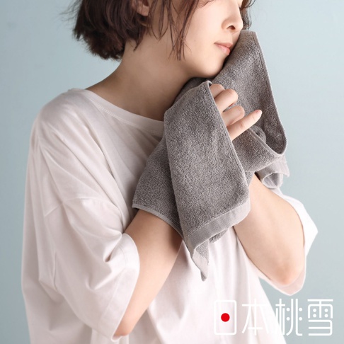 一位女子用灰色毛巾輕輕擦拭臉頰，展現日本桃雪品牌標誌。