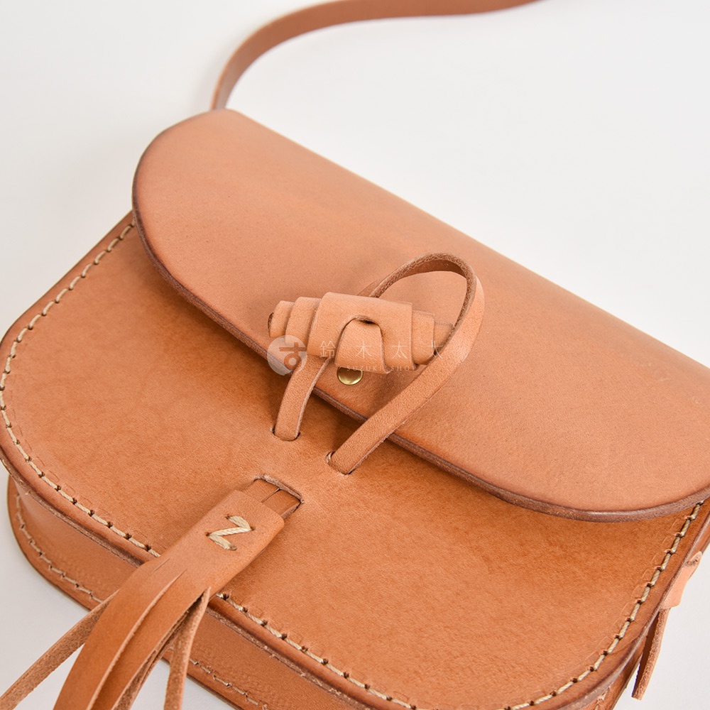 職人手作皮革流蘇側背包，淺棕色，天然皮革材質，帶有手工縫線細節，旋轉鎖扣設計，前方裝飾皮革流蘇。