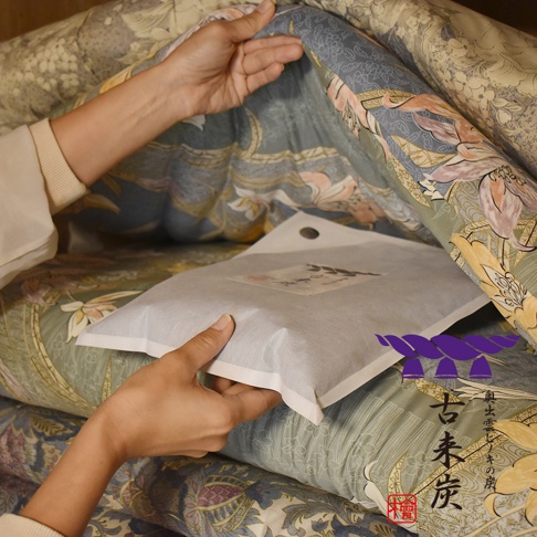 一隻手將灰色無紡布包裝的調濕木炭產品放在帶有花卉圖案的織物上，產品包裝上印有中文字。