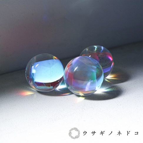 三個透明的合光稜鏡球，表面光滑，折射出彩虹般的光芒，其中一個球體內部呈現藍色立方體。