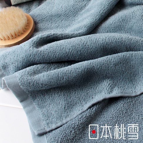 藍灰色毛巾，材質細膩柔軟，質地蓬鬆，呈現細緻的織紋，一角可見品牌標誌。