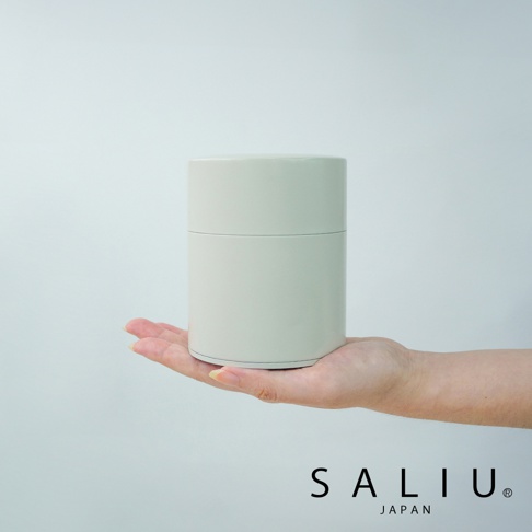 圓柱形淺灰色錫製茶葉罐，罐身簡約無花紋，頂部有蓋，呈放在手掌上，背景為純白色。