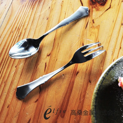 日製錘目紋不鏽鋼水果甜點叉，銀色，以錘擊紋路裝飾，搭配同系列湯匙，置於木紋桌面。