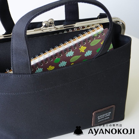 時尚黑色口金手提包，內部有擺放著一本綠葉圖案的筆記本，包袋右下方印有品牌標誌 AYANOKOJI。
