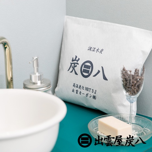 白色方形包裝袋，印有黑色「炭八」字樣及日文說明，內容物為調濕木炭。旁邊有白色洗手盆、銀色皂液器、玻璃杯裝薰衣草及透明盤裝肥皂。