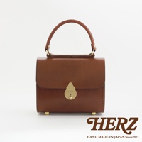 職人手作皮革復古杜勒斯手提包，採用光滑棕色皮革製作，配有金色金屬鎖扣及提把，包底設有四個金色包腳。