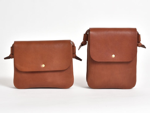 兩款職人手作皮革橫式隨行袋，一款為較扁平的長方形，另一款為較直立的長方形，皆為棕褐色皮革材質，並配有金屬按扣和皮革繫繩。