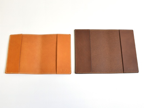 兩件職人手作皮革厚革書套，一件為淺棕色皮革內裡，另一件為深棕色皮革外觀，均配有縫線細節。