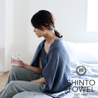 一位女性身穿深藍色2.5層紗材質的浴袍，坐在床邊，手中拿著一杯水。浴袍質地輕柔，有紋理。