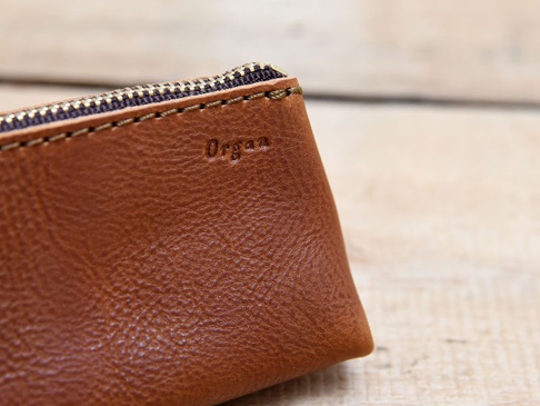 職人手作皮革Organ三角收納筆袋，採用棕色皮革材質，搭配金色拉鍊，表面壓印有「Organ」字樣。