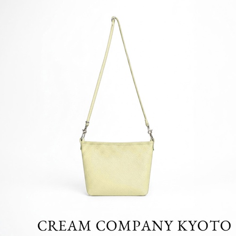 這款 CREAM COMPANY 京都職人手作側背包採用淺黃色粒面牛皮革製成，包身呈現簡約的梯形設計，搭配細長的皮革背帶與金屬掛勾，整體風格輕盈耐用，適合日常外出攜帶。