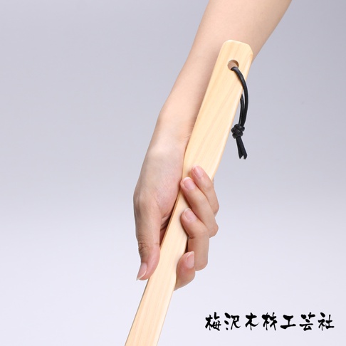 一隻手拿著長款淺木色檜木鞋拔，鞋拔頂端有黑色繩結裝飾。